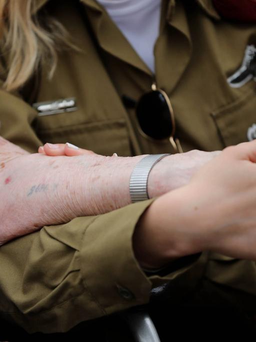 Holocaust-Überlebende Hanna Tessler mit ihrer Enkelin Shira Tessler. Eine israelische Soldatin hält die Hand ihrer Großmutter, die den Holocaust überlebt hat. Auf den Arm hat sie eine tätowierte Nummer. 