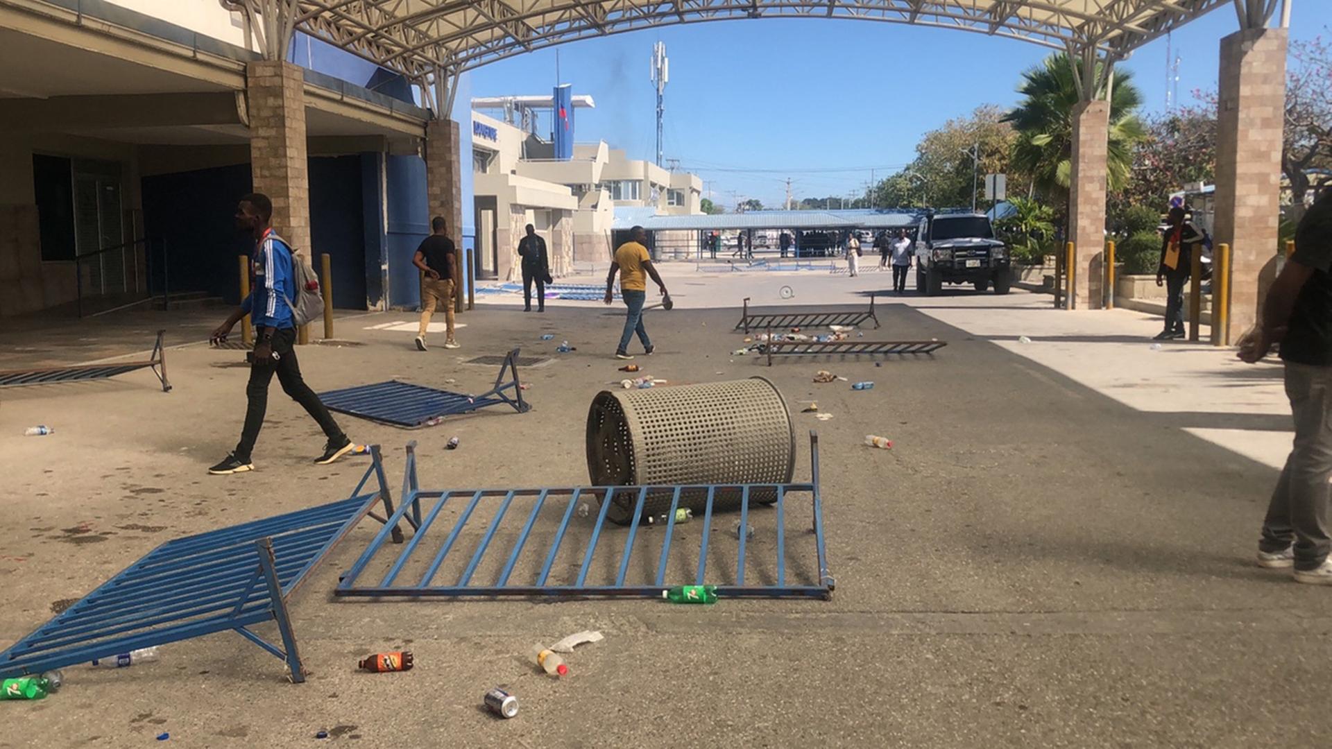Auf einer Straße in Haitis Hauptstadt Port-au-Prince liegen umgestürzte Absperrgitter und ein Mülleimer. Vereinzelte Männer laufen in verschiedene Richtungen. Auf einer Straße in Haitis Hauptstadt Port-au-Prince liegen umgestürzte Absperrgitter und ein Mülleimer. Vereinzelte Männer laufen in verschiedene Richtungen.