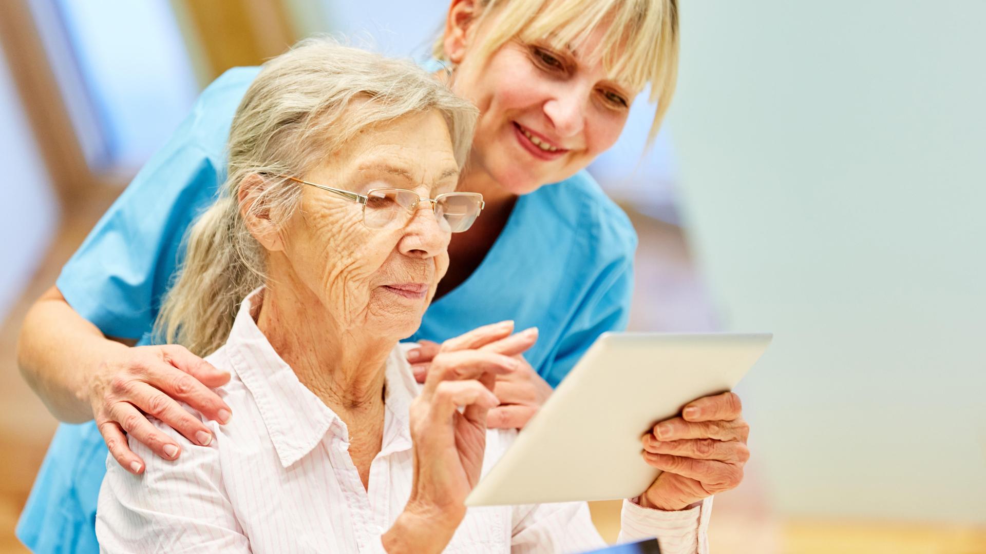Pflegekraft hilft Seniorin mit Tablet-Computer Pflegekraft hilft Seniorin mit Tablet-Computer