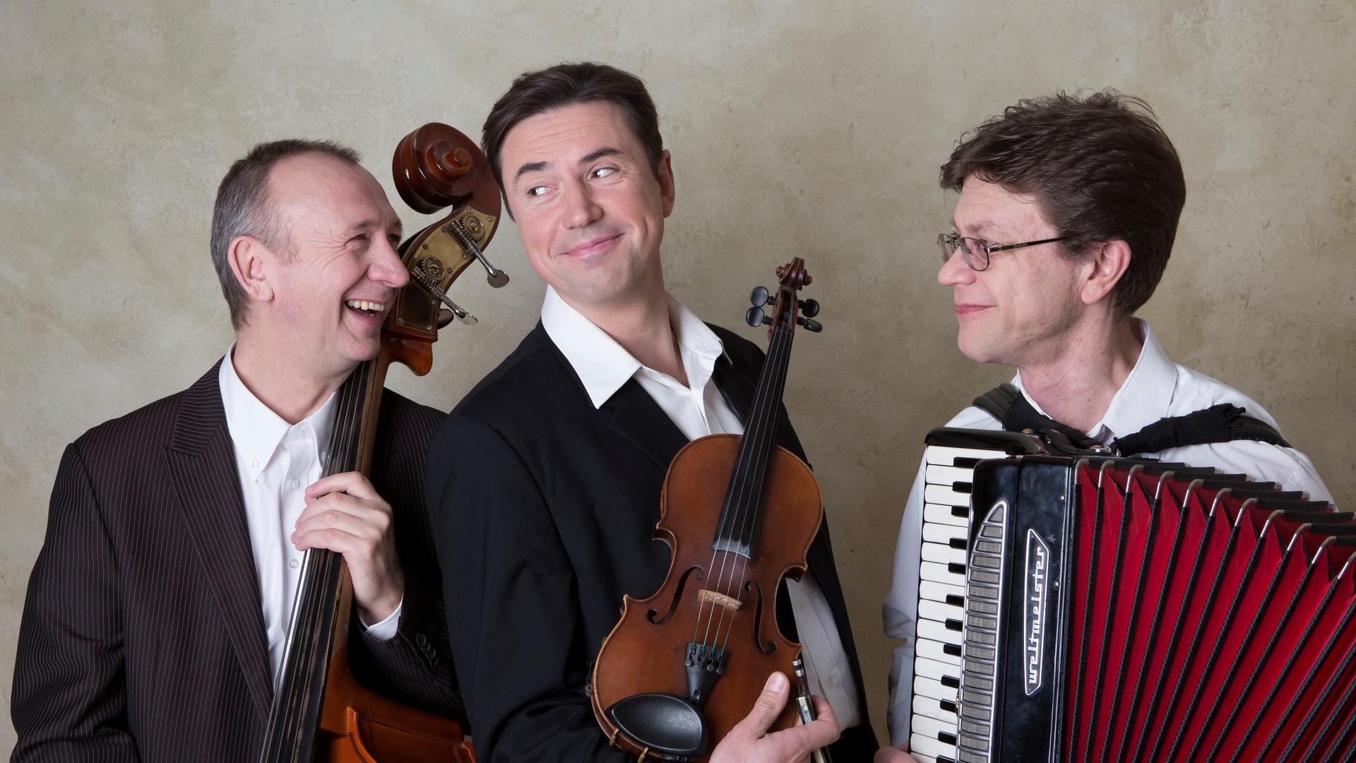 Drei Musiker sind zu sehen, sie lachen und halten ihre Instrumente fest. Drei Musiker sind zu sehen, sie lachen und halten ihre Instrumente fest.