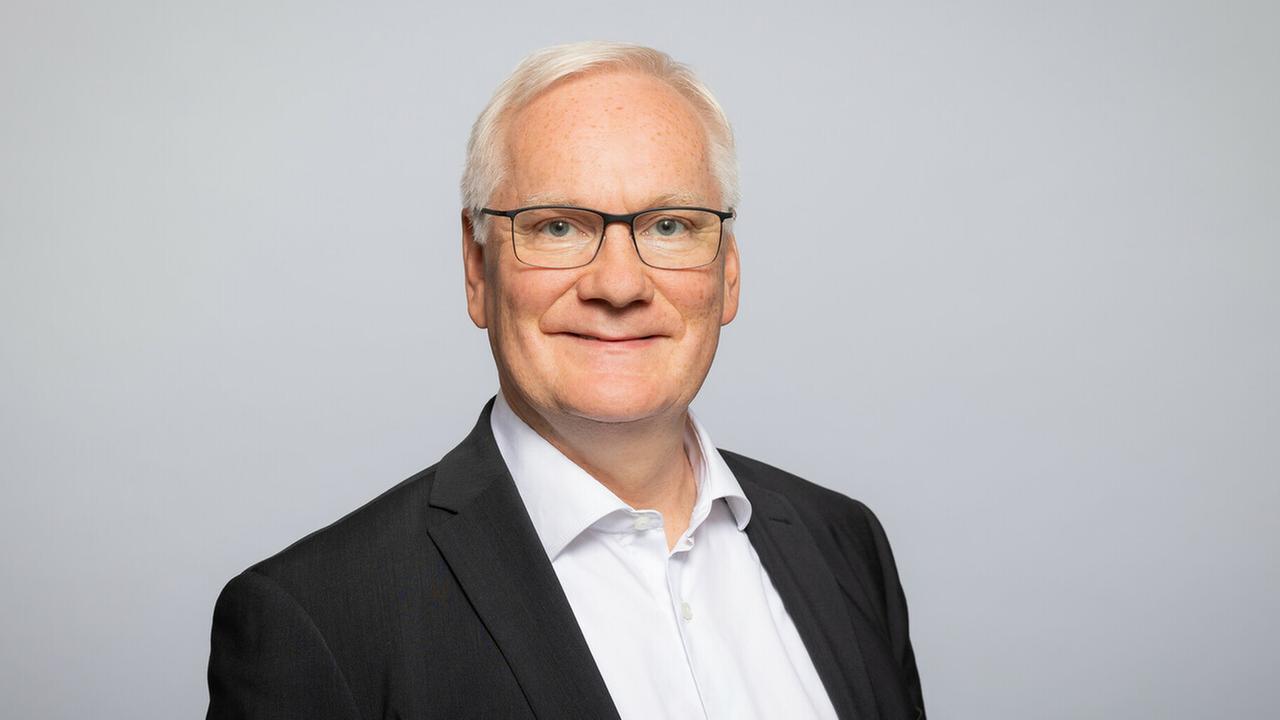 Werner Weinholt, im dunklen Sakko und weißem Hemd, lächelt in die Kamera. Werner Weinholt, im dunklen Sakko und weißem Hemd, lächelt in die Kamera.