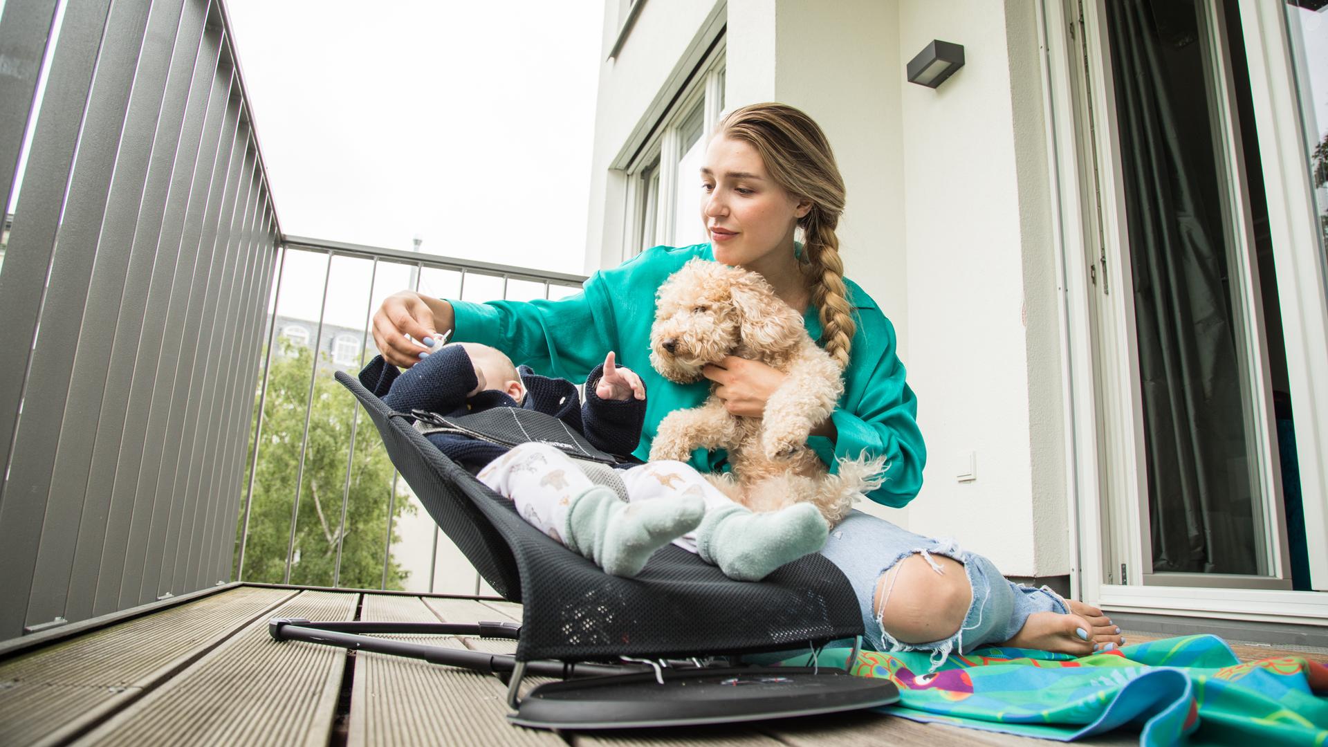 Eine Frau kümmert sich auf dem heimischen Balkon um ihr Kind und den Hund. Eine Frau kümmert sich auf dem heimischen Balkon um ihr Kind und den Hund.