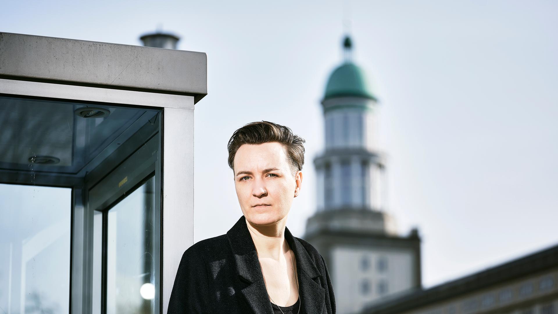Marlen Pelny steht in einer Stadtlandschaft und blickt in die Kamera. Sie hat dunkle, kurze Haare und trägt eine schwarze Jacke und ein schwarzes Oberteil Marlen Pelny steht in einer Stadtlandschaft und blickt in die Kamera. Sie hat dunkle, kurze Haare und trägt eine schwarze Jacke und ein schwarzes Oberteil