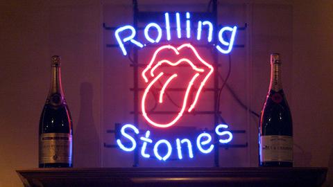 Eine Leuchtreklame mit typischen Rolling Stones Logo einer rausgestreckten Zunge und dem Schrift der Band flankiert von zwei Champagner-Flaschen.