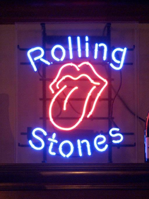 Eine Leuchtreklame mit typischen Rolling Stones Logo einer rausgestreckten Zunge und dem Schrift der Band flankiert von zwei Champagner-Flaschen.