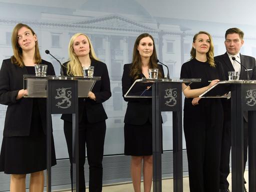 Vier Frauen und ein Mann stehen bei einer Pressekonferenz an Mikrofonen.