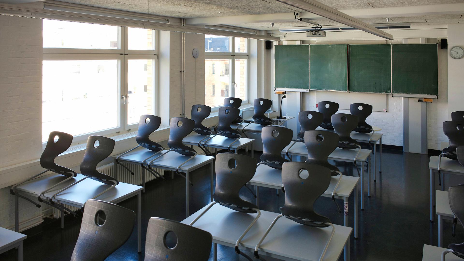 Blick in ein leeres Klassenzimmer mit alter Tafel und hochgestellten Stühlen.