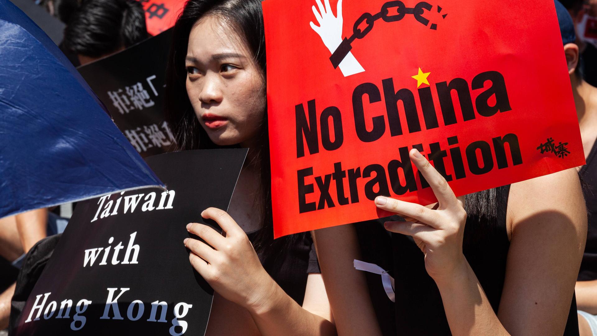 Eine junge Frau hält ein Plakat mit der Aufschrift "Taiwan with Hong Kong", eine andere eins mit "No China Extradition" bei einer Kundgebung in Taipeh, Taiwan, am 16.06.2019
