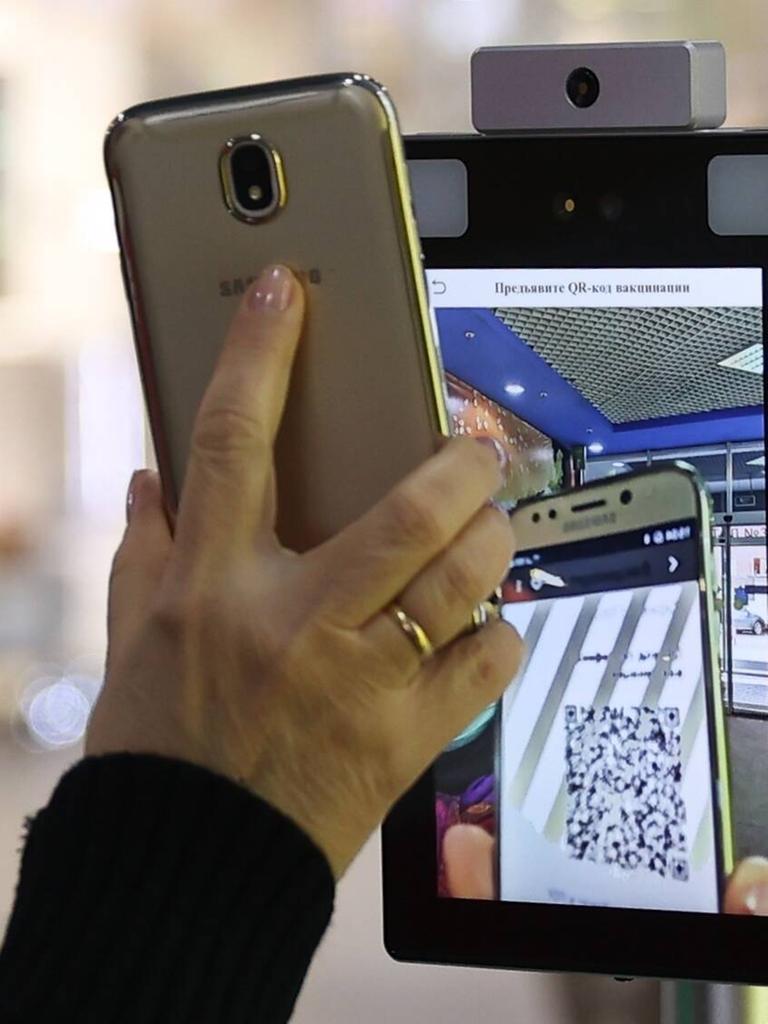 Hand mit Smartphone am Scanner: Eine Frau scannt ihren QR-Impf-Code, bevor sie eine Shoppingmall betritt.
