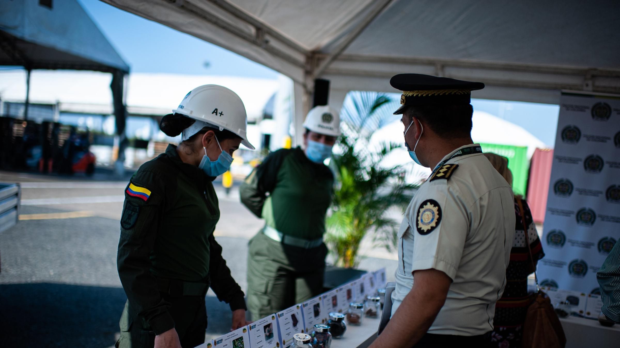 Drei Polizeibeamte treffen im Hafen von Cartagena zusammen, sie stehen vor einem Tisch, auf dem Drogen aufgebaut sind. 