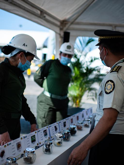 Drei Polizeibeamte treffen im Hafen von Cartagena zusammen, sie stehen vor einem Tisch, auf dem Drogen aufgebaut sind. 