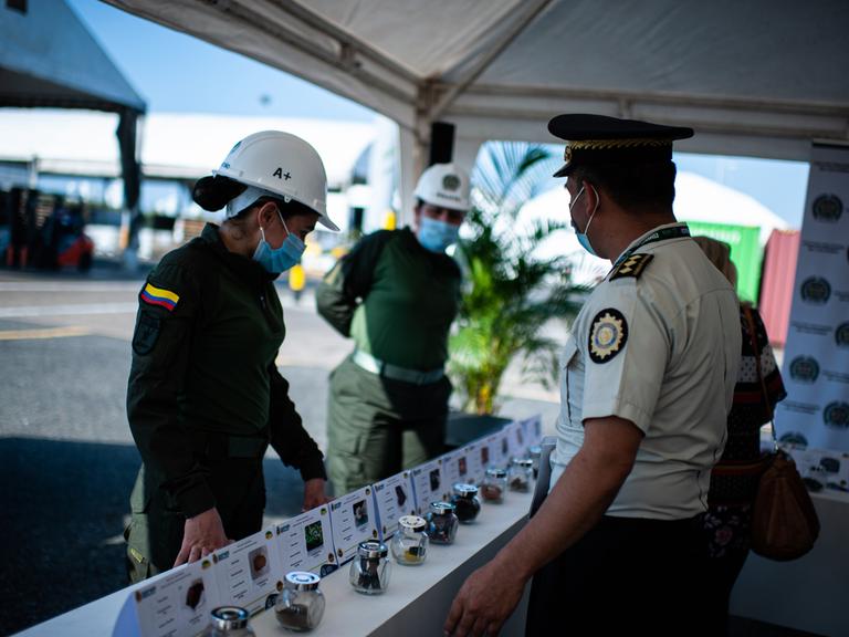 Drei Polizeibeamte treffen im Hafen von Cartagena zusammen, sie stehen vor einem Tisch, auf dem Drogen aufgebaut sind. 