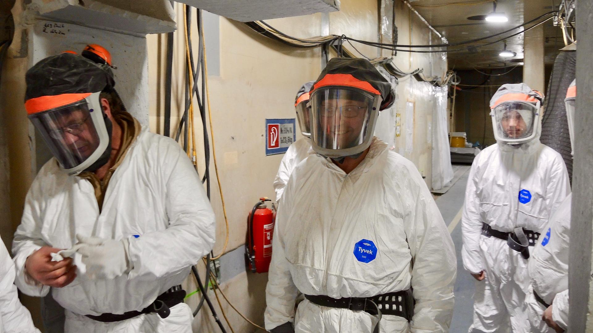 Drei Männer in weißen, strahlensicheren Schutzanzügen und Schutzbrillen gehen durch eine Halle im stillgelegten Atomkraftwerk Greifswald-Lubmin. Drei Männer in weißen, strahlensicheren Schutzanzügen und Schutzbrillen gehen durch eine Halle im stillgelegten Atomkraftwerk Greifswald-Lubmin.