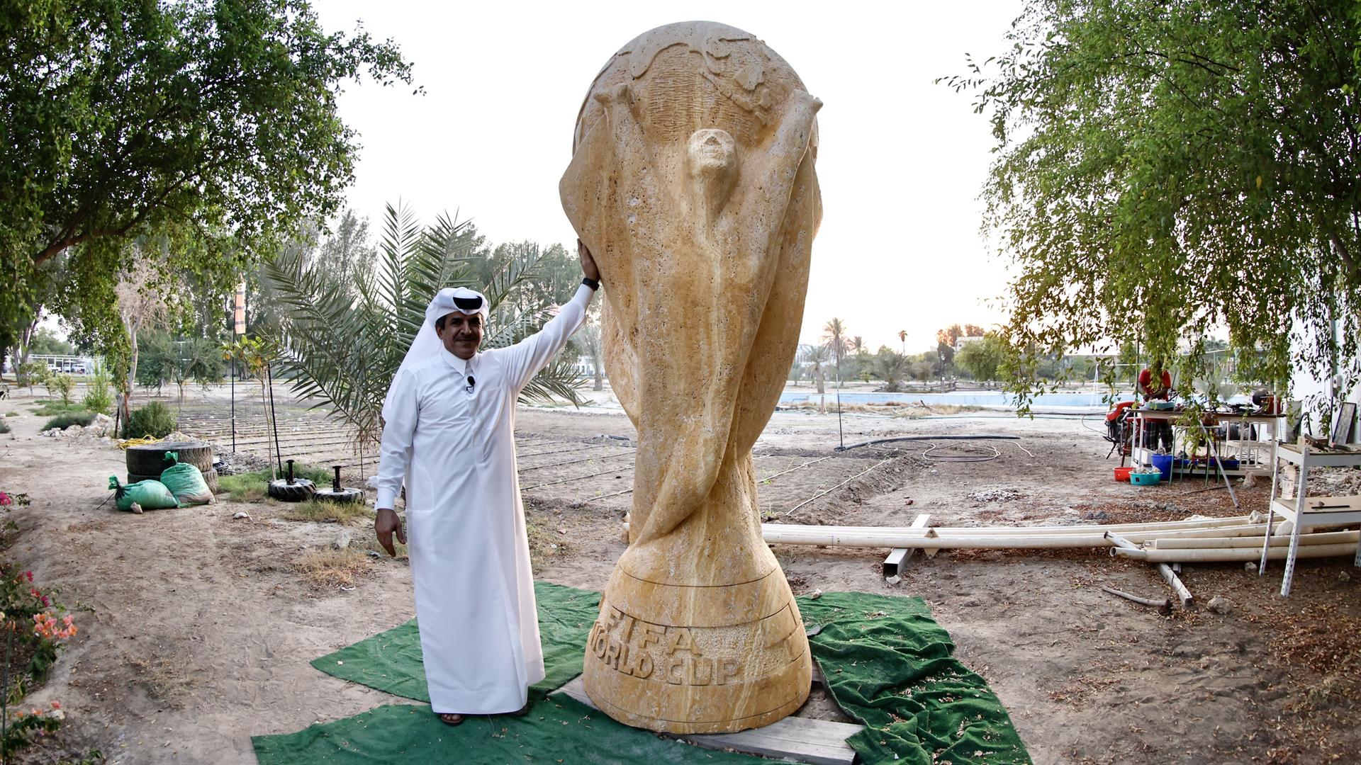Ein Geschäftsmann in weißem Umhang posiert neben einer beinahe drei Meter hohen Skulptur des FIFA-Pokals aus sandfarbenem Travertin. Ein Geschäftsmann in weißem Umhang posiert neben einer beinahe drei Meter hohen Skulptur des FIFA-Pokals aus sandfarbenem Travertin.