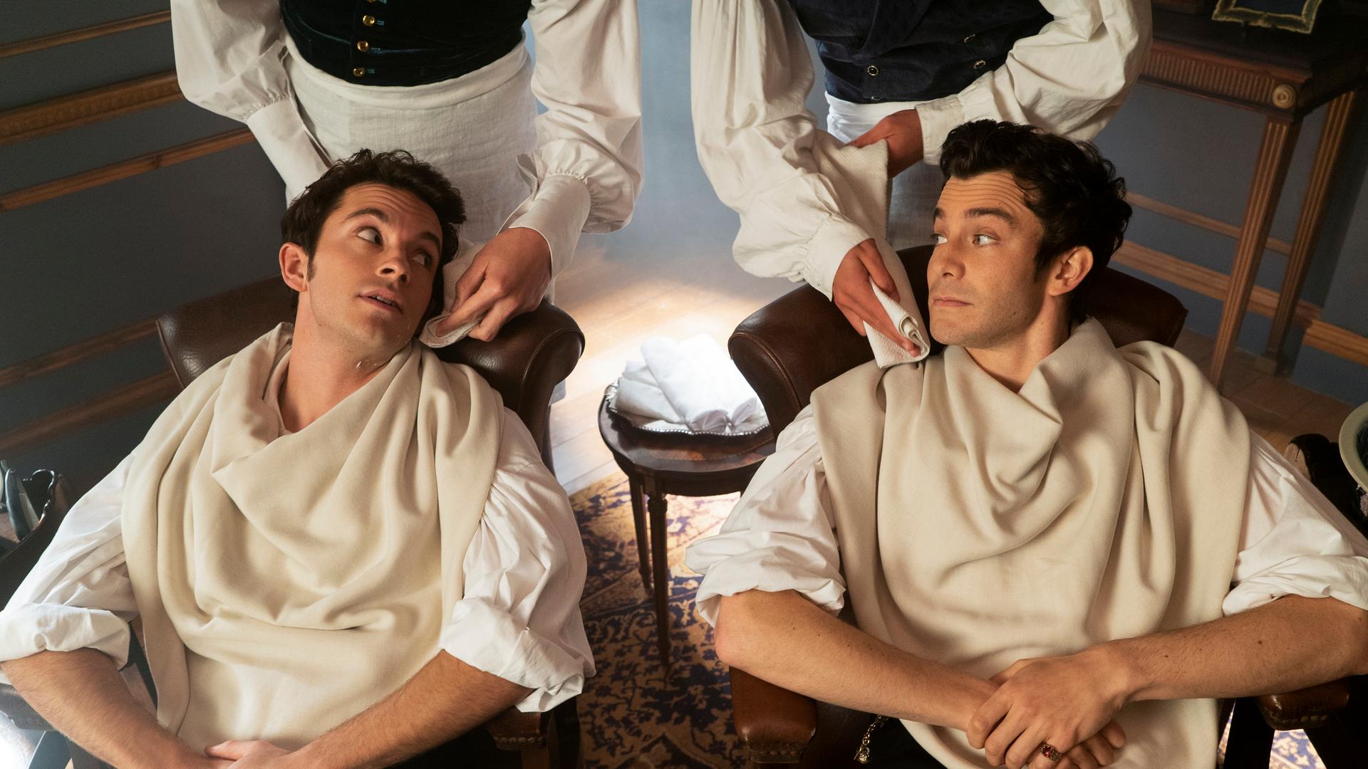 Schauspieler Jonathan Bailey und Luke Thompson sitzen zurückgelehnt auf Stühlen. Schauspieler Jonathan Bailey und Luke Thompson sitzen zurückgelehnt auf Stühlen.