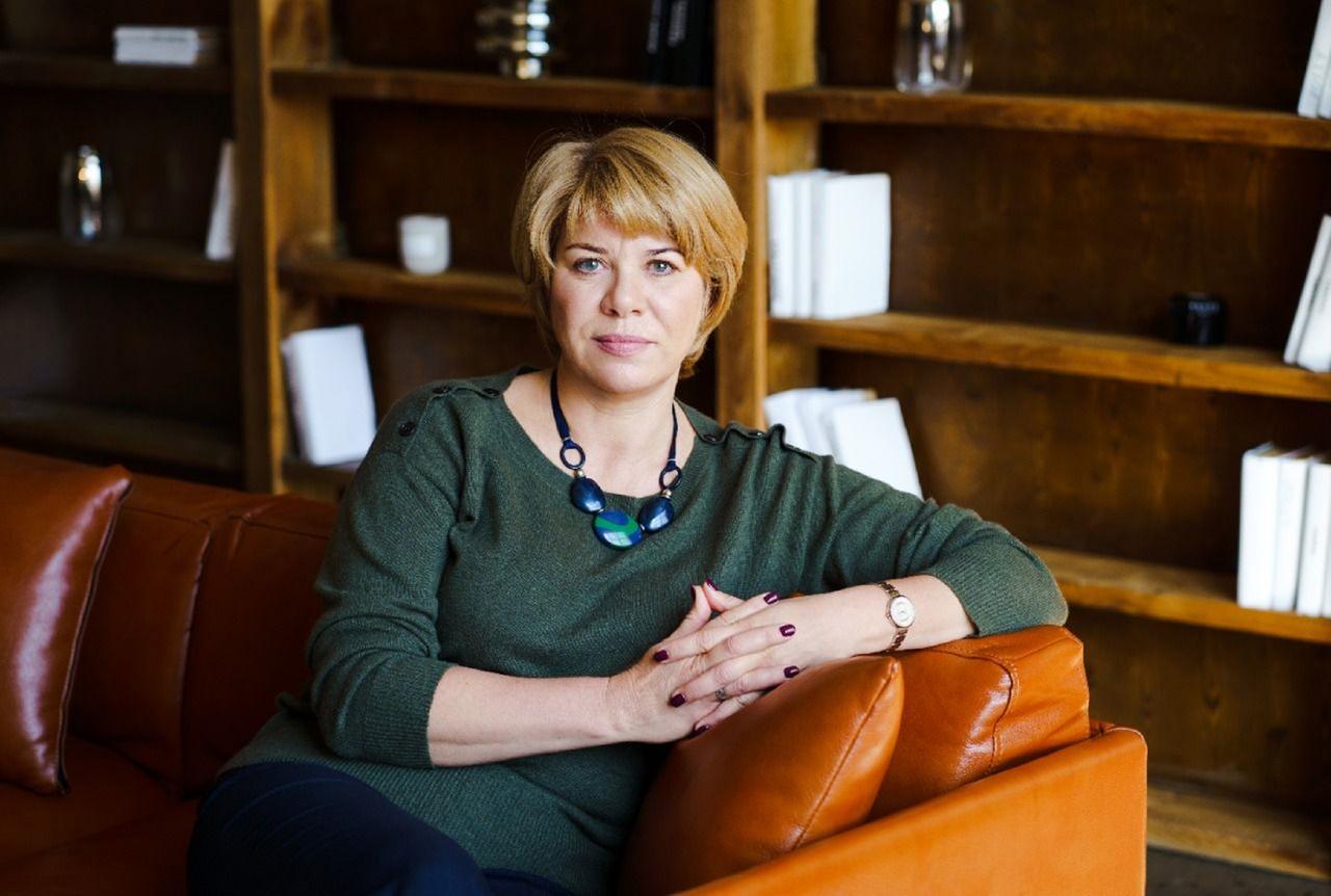 Eine Frau sitzt in einer Bibliothek auf einem Sofa und schaut in die Kamera.
Eine Frau sitzt in einer Bibliothek auf einem Sofa und schaut in die Kamera.