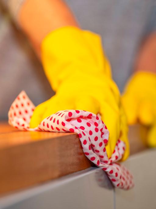 Haushaltshilfe beim Reinigen Person mit gelben Gummihandschuhen wischt mit einem Tuch über eine Arbeitsplatte in einer Küche 