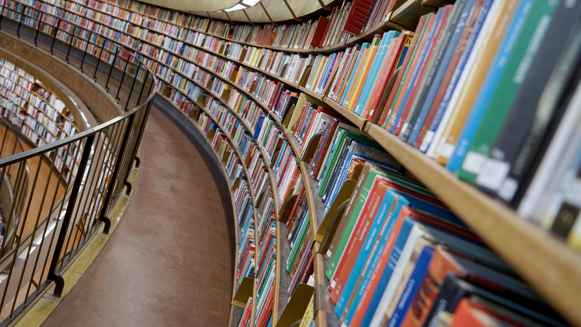 Viele Bücher sortiert in einem lang gezogenen, halbrunden Regal Viele Bücher sortiert in einem lang gezogenen, halbrunden Regal