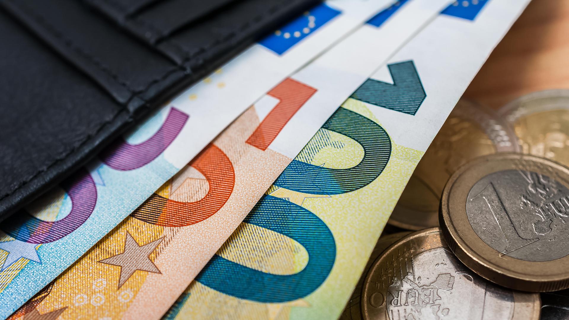 Aus einem Portemonnaie ragen Geldscheine und Münzen der Währung Euro. 