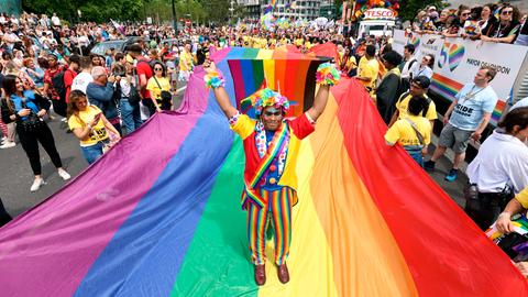 Das Foto zeigt die Pride Parade in London, einer der Teilnehmer steht auf einer Flagge in den Farben des Regenbogens.