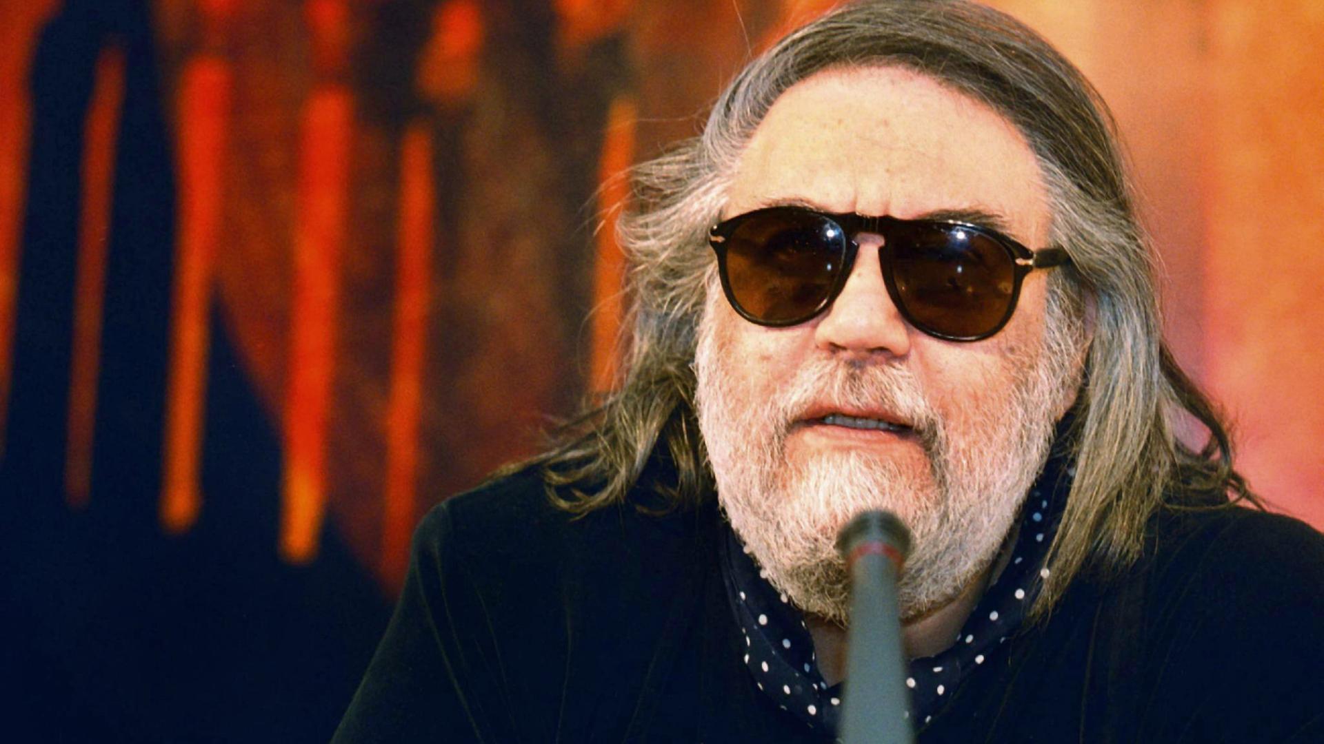 Vangelis trägt eine Sonnenbrille und hat einen Bart. Vangelis trägt eine Sonnenbrille und hat einen Bart.
