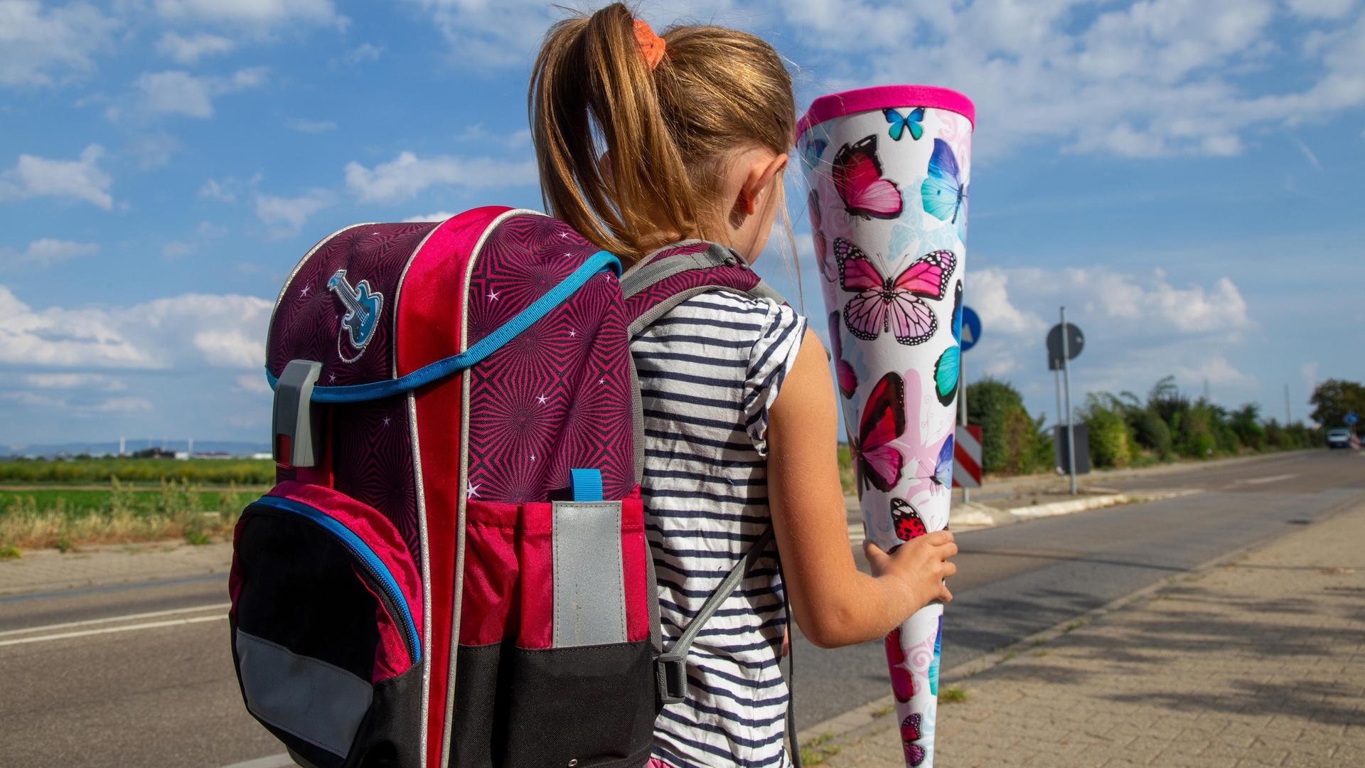Ein Mädchen auf dem Weg zu ihrem ersten Schultag läuft an einer Straße entlang und hält eine Schultüte in der Hand Ein Mädchen auf dem Weg zu ihrem ersten Schultag läuft an einer Straße entlang und hält eine Schultüte in der Hand