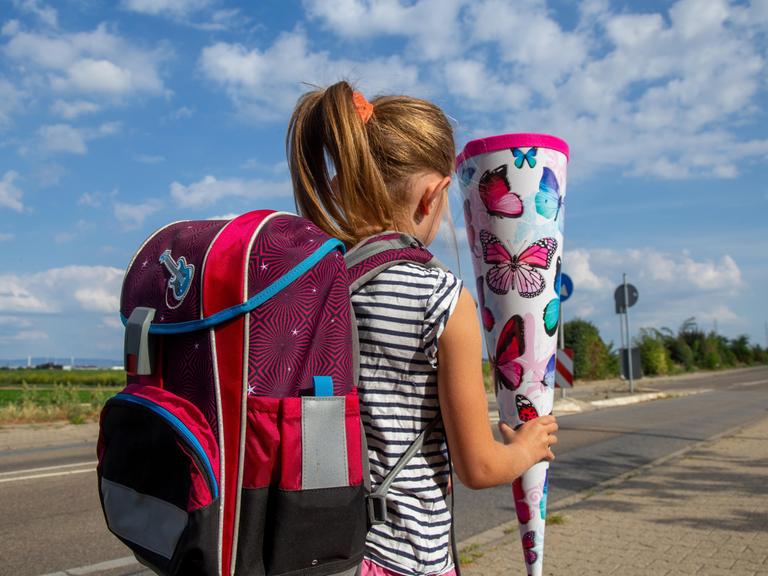 Ein Mädchen auf dem Weg zu ihrem ersten Schultag läuft an einer Straße entlang und hält eine Schultüte in der Hand