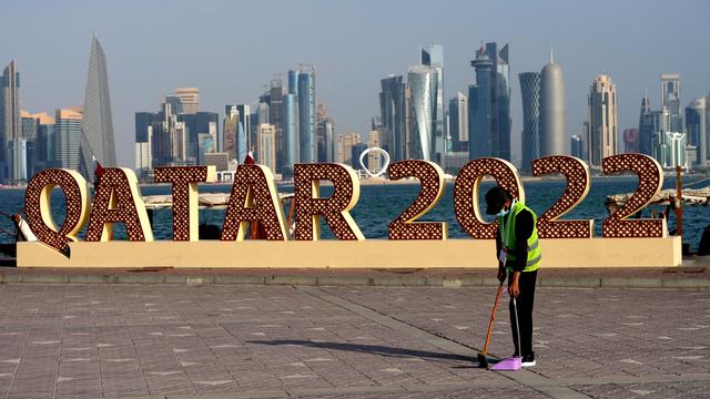 Ein Arbeiter räumt vor einem "Qatar 2022"-Schild Müll weg. Im Hintergrund die Skyline von Doha.
