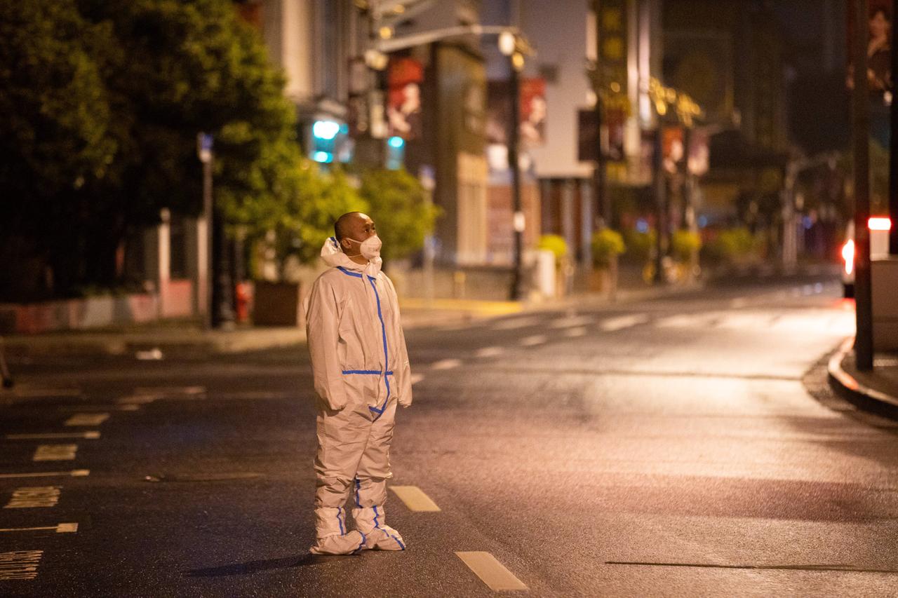 Ein Mann steht in Schutzkleidung auf einer menschenleeren Straße nachts in Schanghai und patrouilliert. Ein Mann steht in Schutzkleidung auf einer menschenleeren Straße nachts in Schanghai und patrouilliert.
