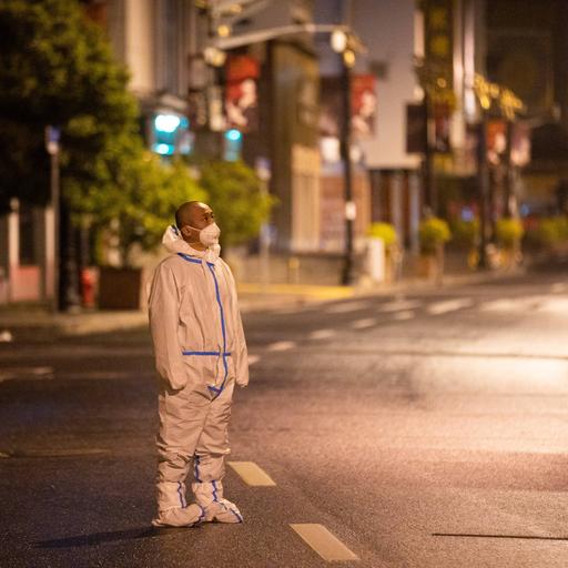 Ein Mann steht in Schutzkleidung auf einer menschenleeren Straße nachts in Schanghai und patrouilliert.