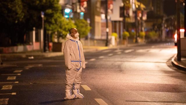 Ein Mann steht in Schutzkleidung auf einer menschenleeren Straße nachts in Schanghai und patrouilliert.