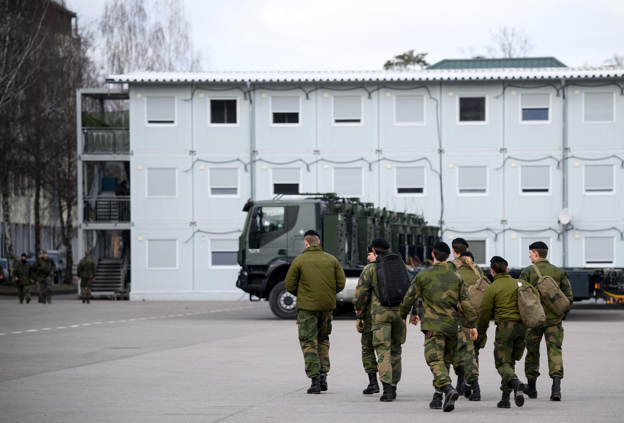 Soldatinnen und Soldaten des von der Bundeswehr angeführten multinationalen Bataillons der NATO Enhanced Forward Presence Battle Group gehen auf dem Militärstützpunkt an Militärlastwagen vorbei.