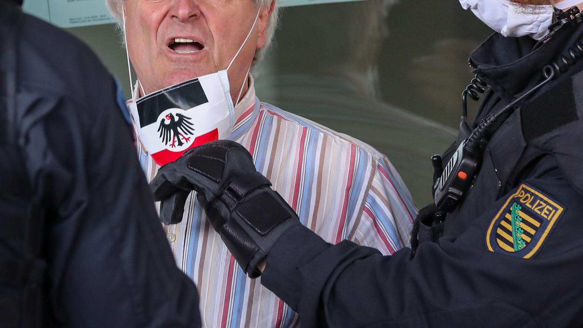 Polizisten nehmen einem Teilnehmer der rechtsextremen Vereinigung Pro Chemnitz einen Mundschutz in den Farben der Reichskriegsflagge und dem Bundesadler ab. Polizisten nehmen einem Teilnehmer der rechtsextremen Vereinigung Pro Chemnitz einen Mundschutz in den Farben der Reichskriegsflagge und dem Bundesadler ab.