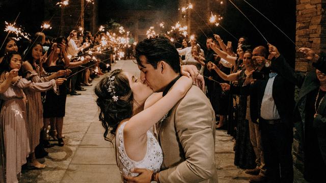Ein Hochzeitspaar küsst sich, während die Gäste dahinter Spalier stehen und brennende Wunderkerzen halten. 