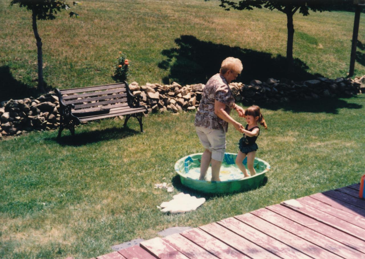 Eine Großmutter spielt mit Ihrer Enkelin draußen auf einer grünen Wiese in einem Planschbecken. Das Foto hat eine Retro-Anmutung. Es wurde vermutlich in den 1970er-Jahren aufgenommen. Eine Großmutter spielt mit Ihrer Enkelin draußen auf einer grünen Wiese in einem Planschbecken. Das Foto hat eine Retro-Anmutung. Es wurde vermutlich in den 1970er-Jahren aufgenommen.