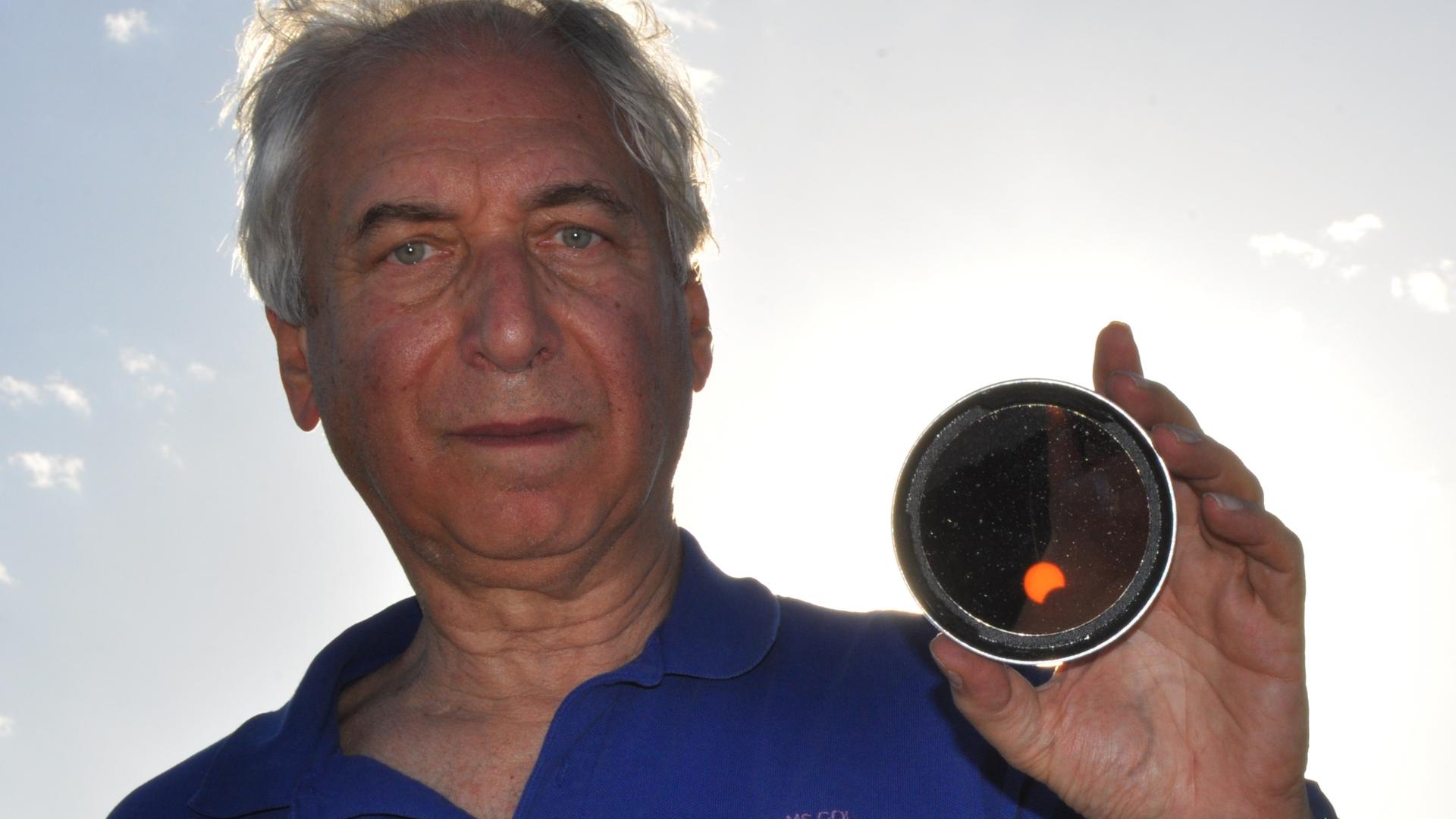 Jay Pasachoff hält einen kleinen Spiegel in der Hand, in der man eine partielle Sonnenfinsternis sehen kann.