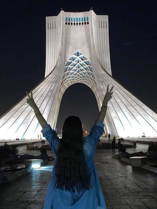 Eine junge Frau ohne Hijab mit offenen Haaren macht das Victoryzeichen mit ihren beiden Händen vor dem Azadi Turm in Teheran, 17.November 2022.