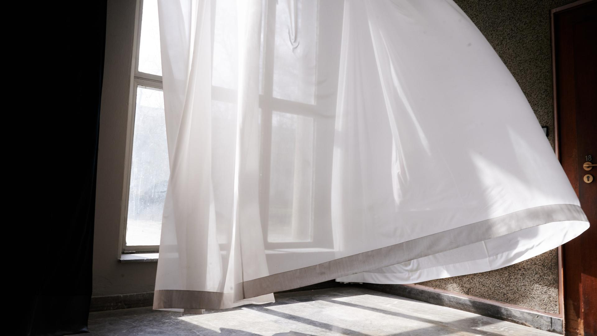Der Wind lässt einen Vorhang vor einem Fenster wehen. Der Wind lässt einen Vorhang vor einem Fenster wehen.