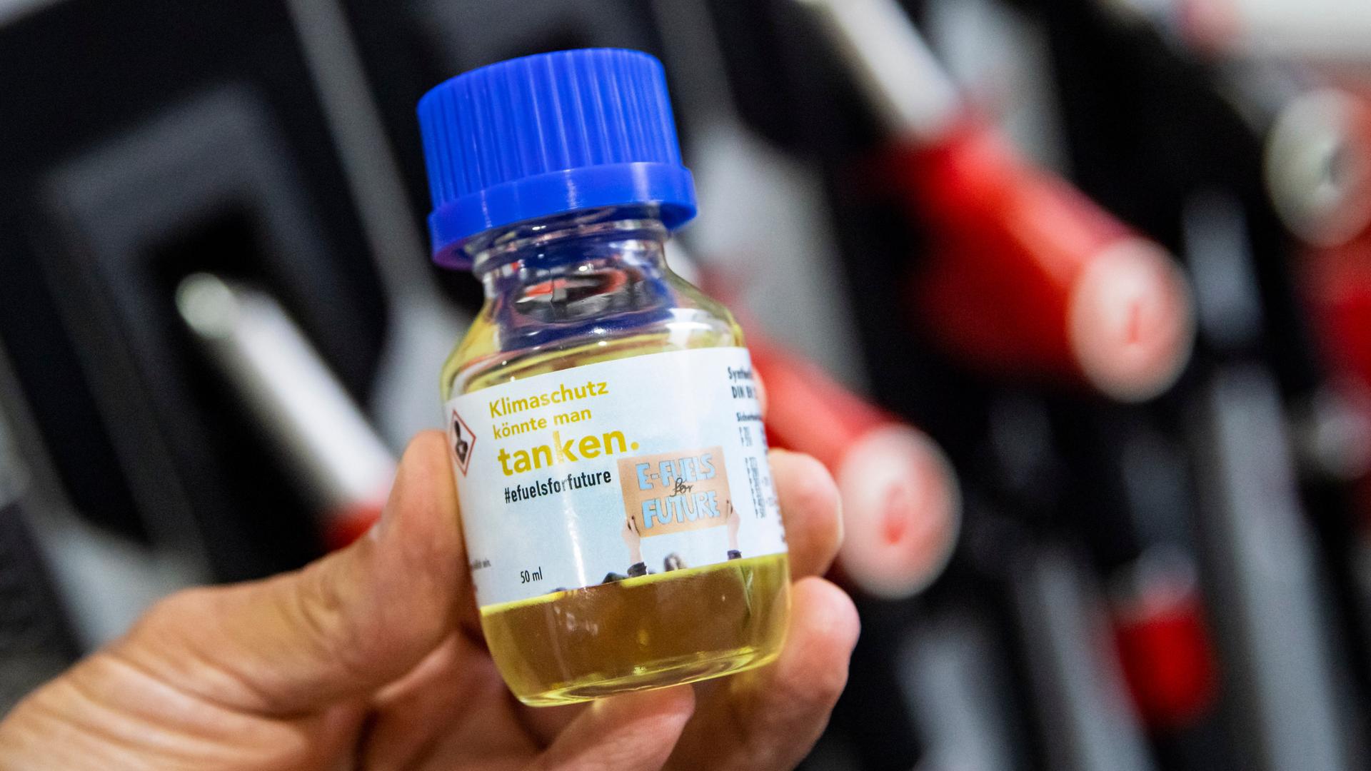 Eine Flasche mit der Aufschrift "Klimaschutz könnte man Tanken - E-Fules for Future" wird vor einer Zapfsäule an einer Tankstelle gehalten. Eine Flasche mit der Aufschrift "Klimaschutz könnte man Tanken - E-Fules for Future" wird vor einer Zapfsäule an einer Tankstelle gehalten.