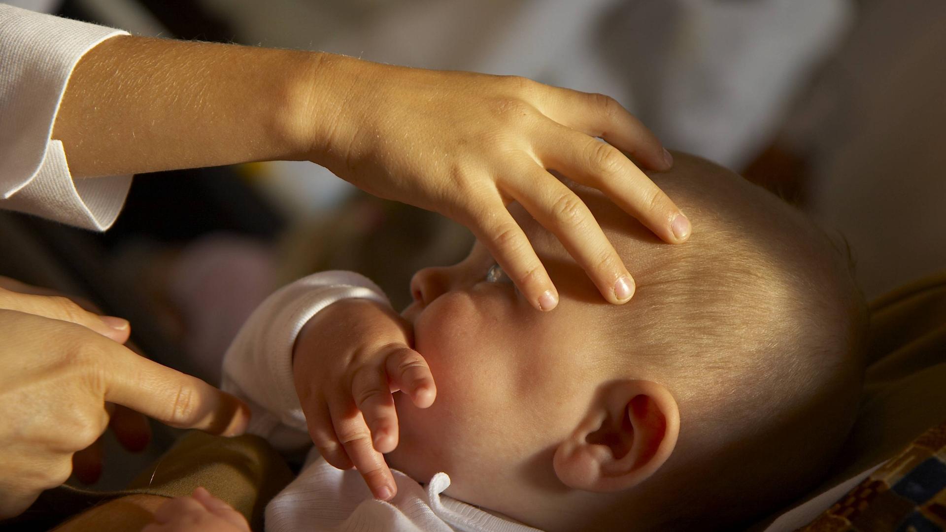 Ein Baby während der Taufe, eine Hand erteilt den Segen auf dem Kopf. Ein Baby während der Taufe, eine Hand erteilt den Segen auf dem Kopf.