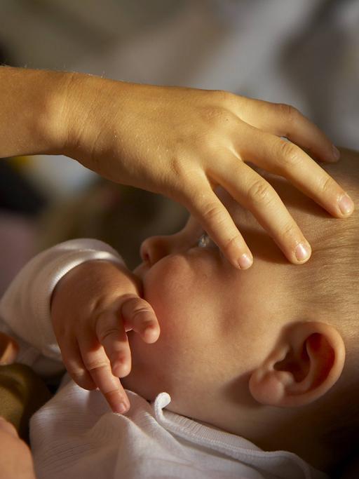 Ein Baby während der Taufe, eine Hand erteilt den Segen auf dem Kopf.