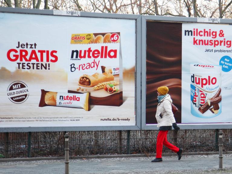 Eine Fußgängerin geht bei Kälte an einem Großplakat mit Webung für Duplo und Nutella B-ready von Ferrero vorbei.