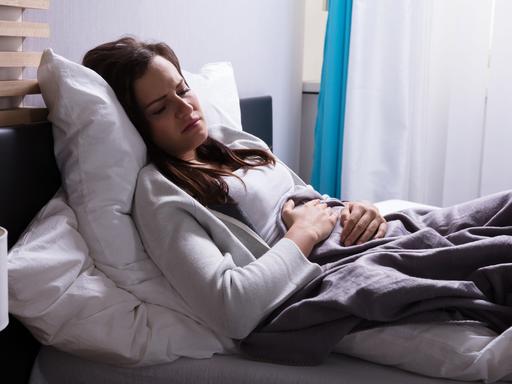 Eine Frau liegt mit Menstruationsschmerzen im Bett.