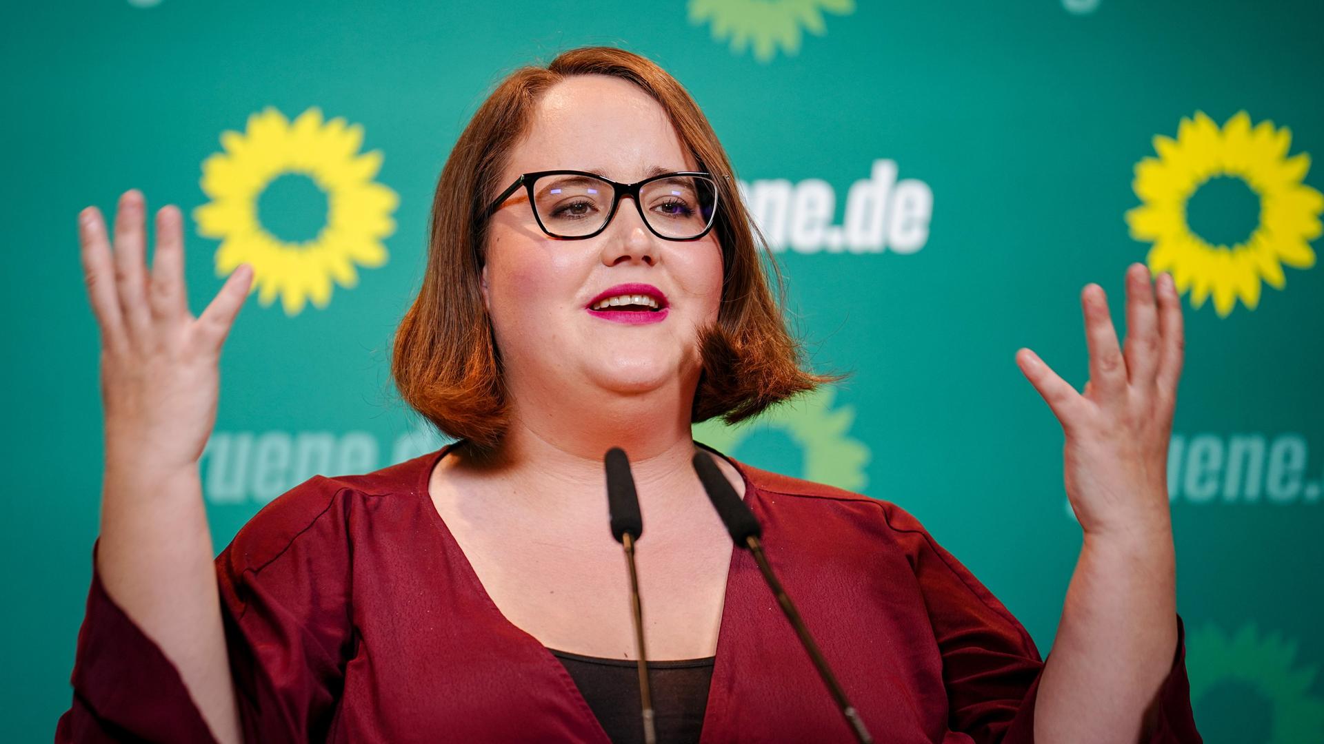Ricarda Lang, Bundesvorsitzende von Bündnis 90/Die Grünen gestikuliert während einer Rede. Vor ihr stehen Mikrofone, hinter ihr sind Sonnenblumen und der Schriftzug "grüne.de" zu sehen. Ricarda Lang, Bundesvorsitzende von Bündnis 90/Die Grünen gestikuliert während einer Rede. Vor ihr stehen Mikrofone, hinter ihr sind Sonnenblumen und der Schriftzug "grüne.de" zu sehen.