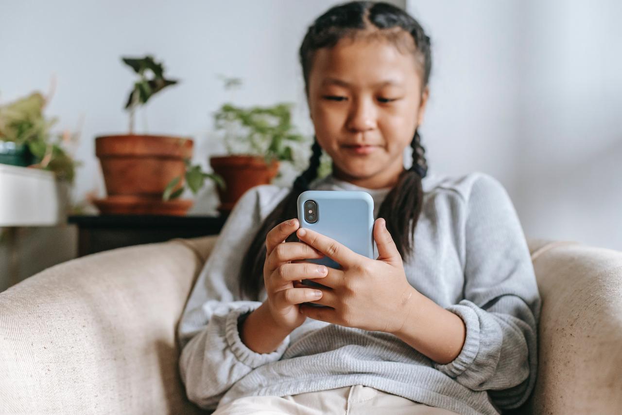 Ein Mädchen sitzt auf einem Sofa und schaut auf ihr Smartphone. Ein Mädchen sitzt auf einem Sofa und schaut auf ihr Smartphone.