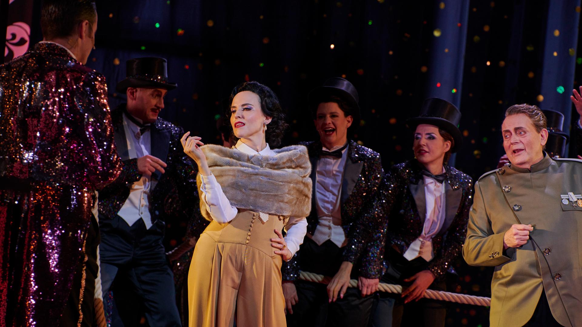 Szenenbild der Jazz-Operette "Die lustige Witwe": Die Schauspielerin Rebecca Nelsen posiert in ihrer Rolle als Hanna Glawari in luxuriös anmutender Kleidung vor dem Ensemble. Szenenbild der Jazz-Operette "Die lustige Witwe": Die Schauspielerin Rebecca Nelsen posiert in ihrer Rolle als Hanna Glawari in luxuriös anmutender Kleidung vor dem Ensemble.