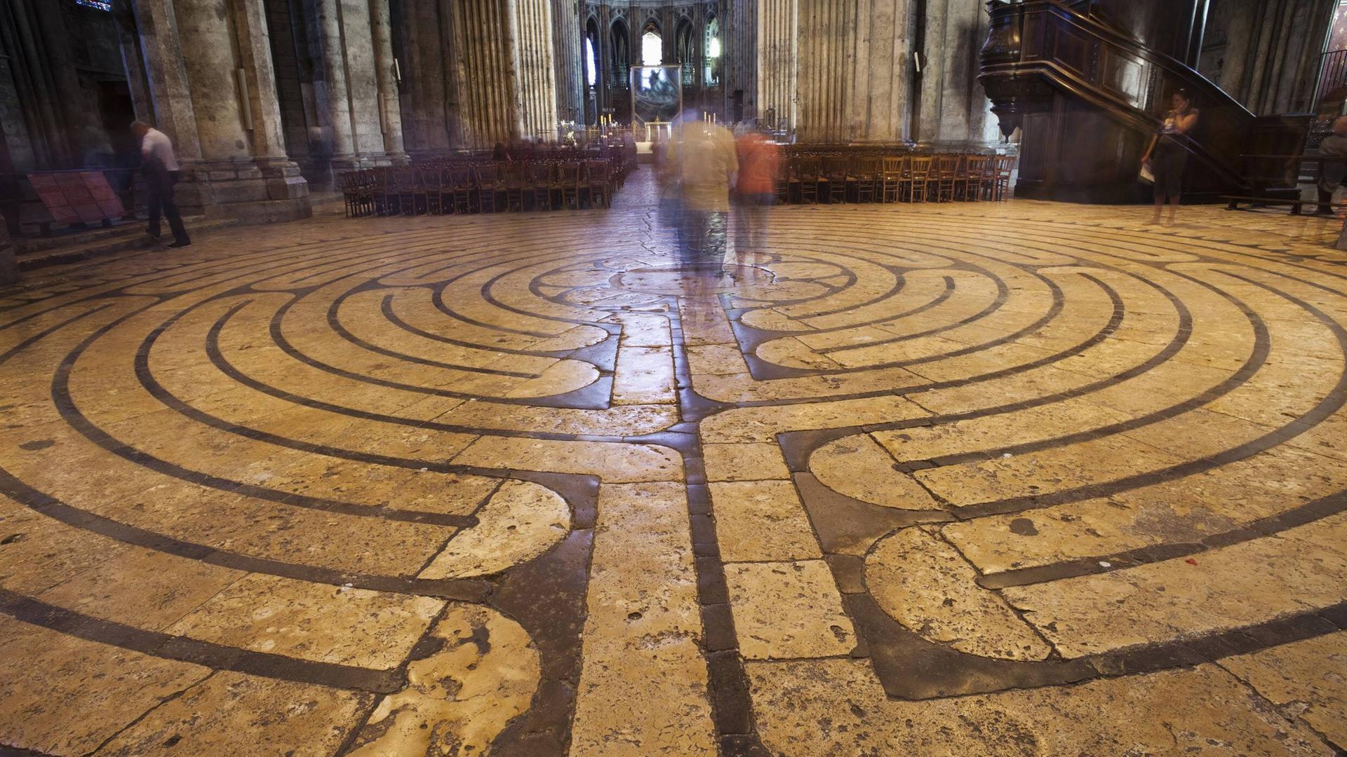 Das Foto zeigt das im Steinboden der Kathedrale von Chartres zu sehende Labyrinth. Im Hintergrund der Altar, unscharf sind zwei Menschen auf dem Labyrinth zu erkennen, die dort gehen. Das Foto zeigt das im Steinboden der Kathedrale von Chartres zu sehende Labyrinth. Im Hintergrund der Altar, unscharf sind zwei Menschen auf dem Labyrinth zu erkennen, die dort gehen.