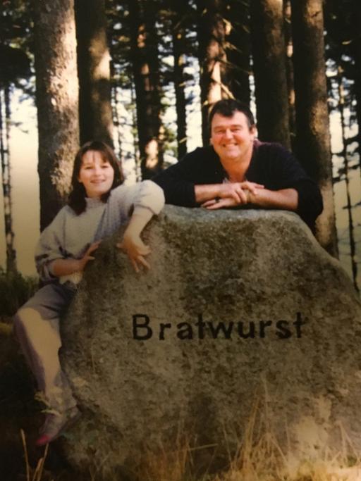 Eine Frau und ein Mann stehen hinter einem Felsen, auf dem "Bratwurst" steht.
