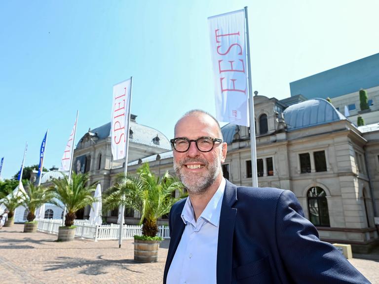 Auf dem Bild ist Festpielhaus Intendant Benedikt Stampa zu sehen, wie er freundlich in die Kamera lächelt. 
