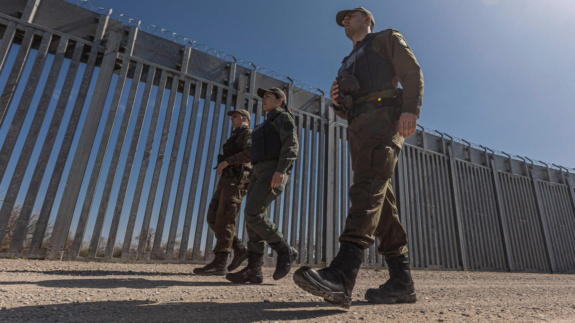 Drei Grenzschützende patrouillieren am Grenzzaun, der Griechenland von der Türkei trennt. 